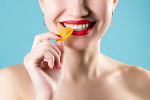 istock girl smiles, bites and pulls a yellow condom. Close-up 1217327701
