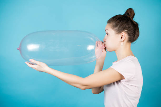 Side view of a young girl inflating a condom Side view of a young girl inflating a condom Blue background condom photos stock pictures, royalty-free photos & images