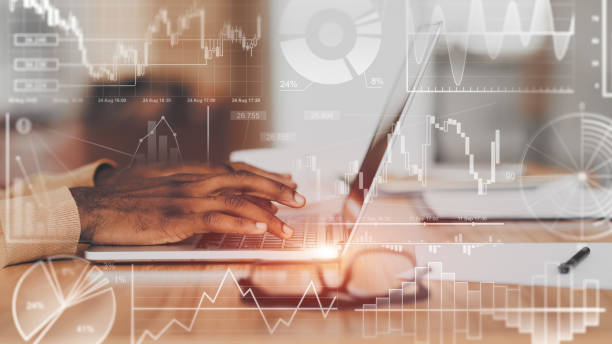 istock Unrecognizable African American employee using laptop in office, collage with financial info on transparent screen 1217330142