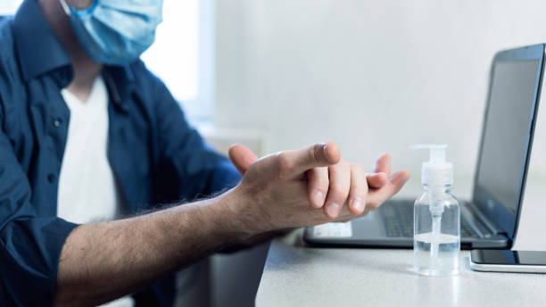 istock Man In Mask Sterilizing Hands Working Remotely At Home, Cropped 1217331056