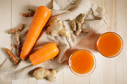 Carrots, ginger, turmeric detox fresh juice on wooden background. Healthy vegetarian food concept.