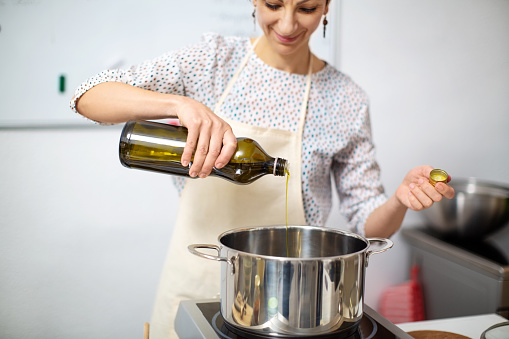 Female chef adding oil in a cooking pan on stove. Woman preparing food in the kitchen.