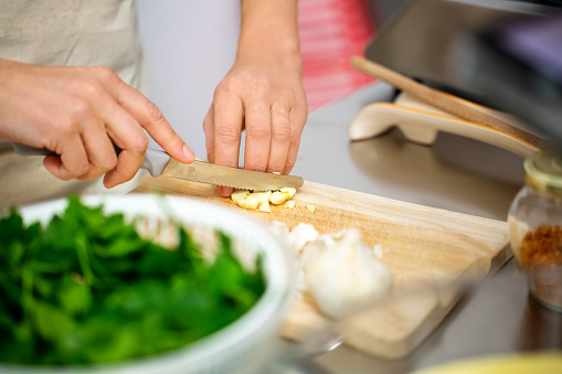 Hands of a female chef chopping vegetables on cutting board. Woman cooking food in kitchen, cutting ingredients with knife.
