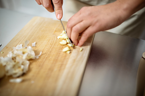 Hands of a woman cutting garlic on kitchen counter. Female chef cooking in kitchen, cutting ingredients with knife.