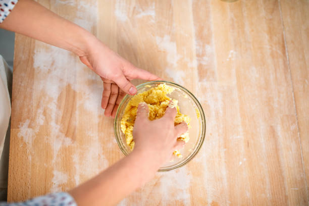 Point of view shot of a female chef's hands kneading dough in a glass bowl. Woman hands preparing dough for pasta on wooden table.