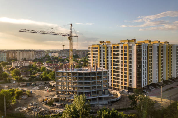 istock Apartment or office tall building under construction. Brick walls, glass windows, scaffolding and concrete support pillars. Tower crane on bright blue sky copy space background. 1217347760