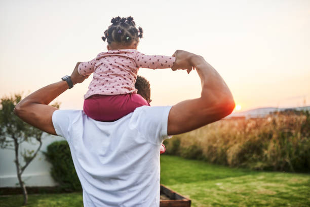 Babies are a gift from above Shot of an adorable baby girl having fun with her dad in their backyard on shoulders stock pictures, royalty-free photos & images