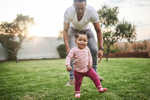 Taking life step by step Shot of an adorable baby girl having fun with her dad in their backyard first steps stock pictures, royalty-free photos & images