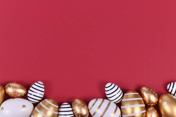 istock Flat lay with golden and white easter eggs painted with stripes and dots at bottom of dark red background with blank copy space 1217349507