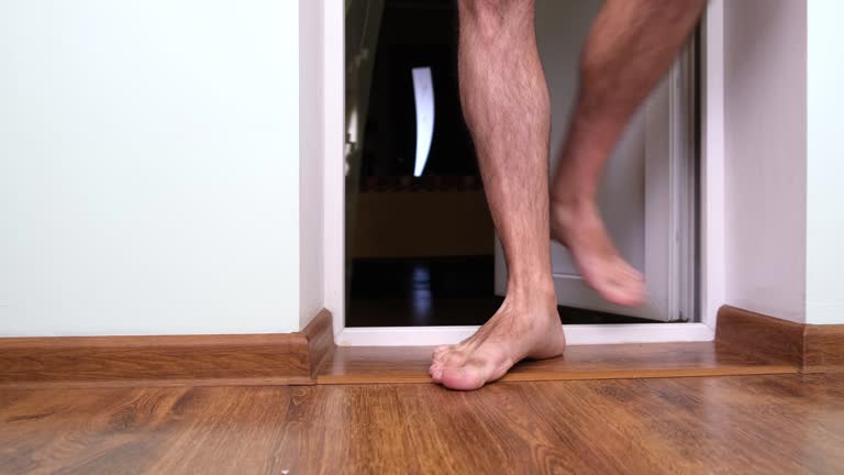 Frumpy man with hairy legs in shorts barefoot crosses the threshold, enters the balcony of a Flat.