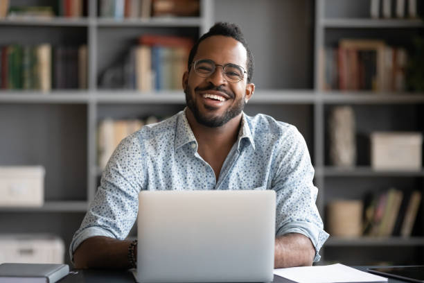 verticale de l’homme biracial de sourire travaillant sur l’ordinateur portatif - looking at camera smiling desk isolated photos et images de collection