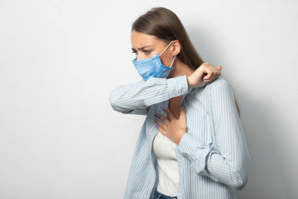 Girl Coughing Into Elbow Wearing Mask Standing Over White Background Coronavirus Respiratory Hygiene. Sick Girl Coughing Into Elbow Wearing Protective Medical Mask Having Covid-19 Pneumonia Standing Over White Background. Copyspace symptom photos stock pictures, royalty-free photos & images