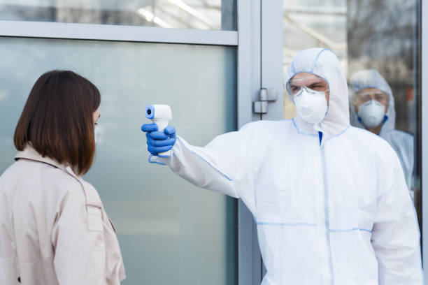 istock Medical worker in virus protective suit measuring temperature 1217354480