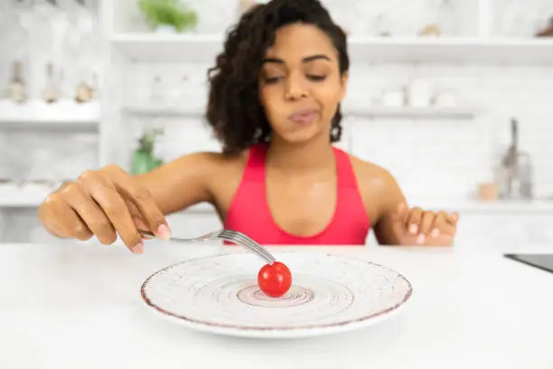 Photo of Depressed afro woman looking at tiny tomato on a plate