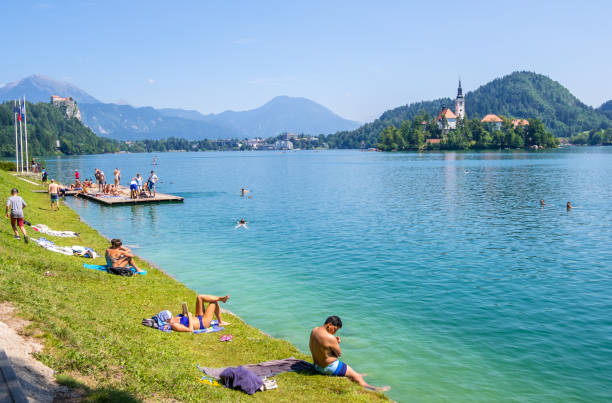 People relax on the beach of the lake Bled, Slovenia Bled, Slovenia - August 10, 2019: People relax on the shores of Lake Bled on background a beautiful landscape with church on a small island, Slovenia gorenjska stock pictures, royalty-free photos & images