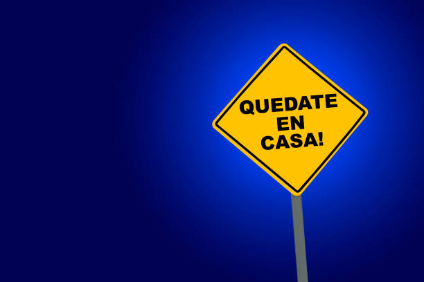 Digitally generated image showing QUEDATE EN CASA on a yellow warning road sign against blue background