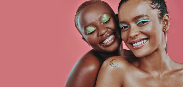 Shot of two beautiful young women posing together against a pink background