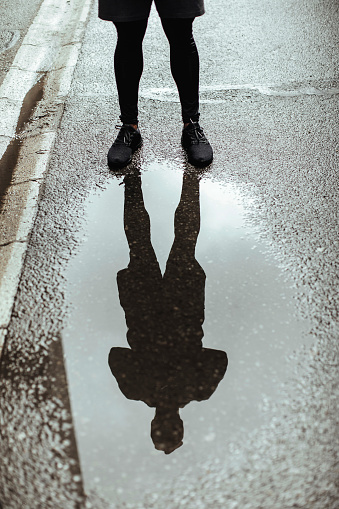 Man in sport clothing standing in street near a puddle with a reflection of him
