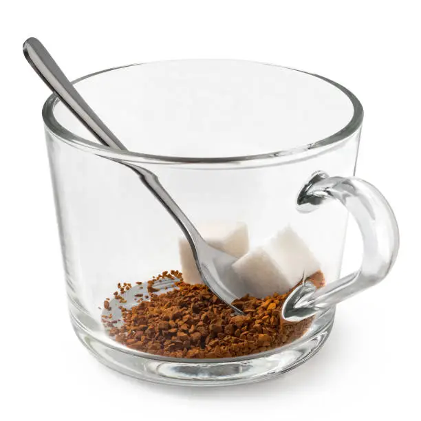 Dry instant coffee and cubes of sugar in a glass mug with metal spoon isolated on white.