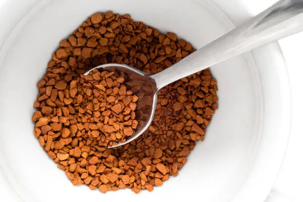 Dry instant coffee in a white ceramic cup with metal spoon. Top view.