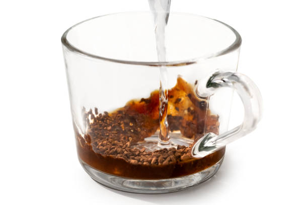 Instant coffee. Pouring hot water onto instant coffee in grass mug isolated on white. Partially dissolved coffee. instant coffee stock pictures, royalty-free photos & images