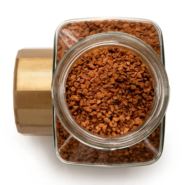 Open glass jar of dry instant coffee next to a golden lid isolated on white. Top view.