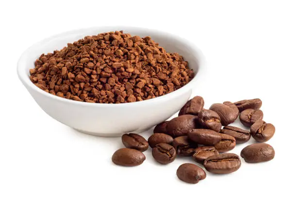 Dry instant coffee in a white ceramic dish next to coffee beans isolated on white.