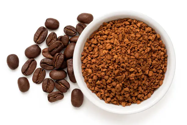Dry instant coffee in a white ceramic dish next to coffee beans isolated on white. Top view.