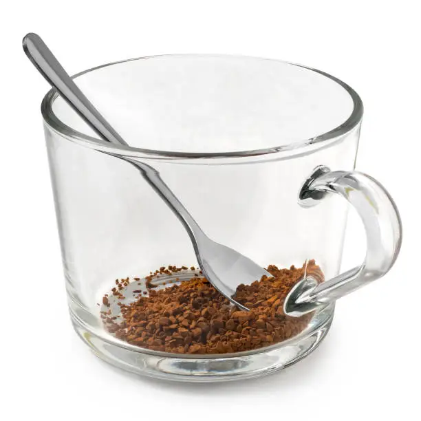 Dry instant coffee in a glass mug with metal spoon isolated on white.