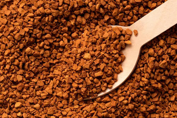 Background detail of dry instant coffee with wooden spoon.