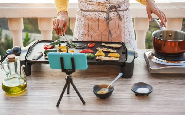 Young woman chef cooking outdoor while streaming online for webinar masterclass lesson at home - Girl making videos preparing vegetarian meal on her patio terrace - Food concept - Focus on hands
