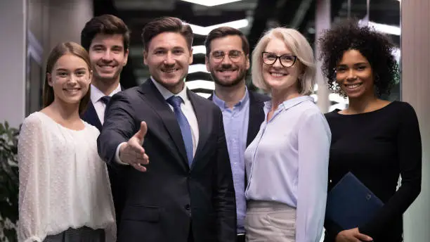 Group portrait of diverse businesspeople stand together meeting newbie to international team, smiling multiracial colleagues stretch hand welcome new worker at workplace, employment concept