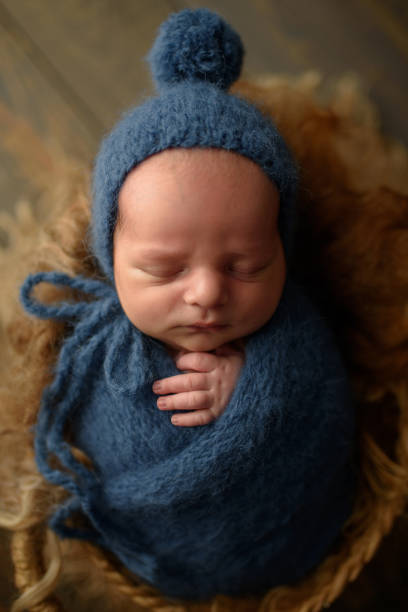 istock Newborn boy in a blue knitted hat and winding sleeps in a basket on a wooden background. 1217363473