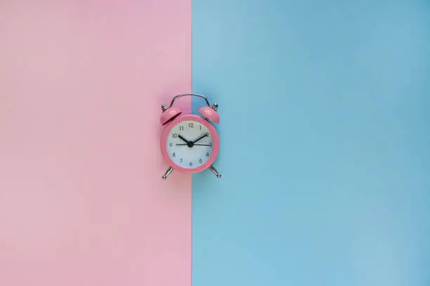 Ringing twin bell vintage alarm clock isolated on pink and blue background with copy space. Rest hours time, goodmorning, new life time. Top view, flat lay style