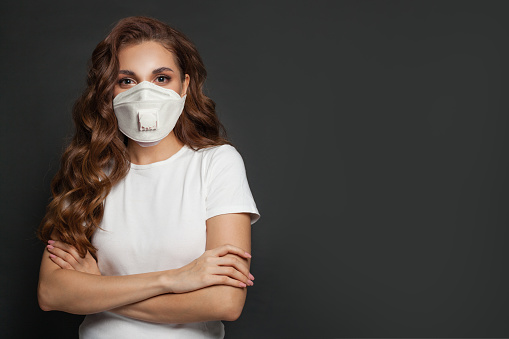 Confident woman in medical safety face mask on dark gray background. Woman in medical mask portrait