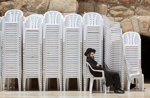 Jerusalem, Israel - May 8, 2019 Religious jewish man is sitting in front of stack of chairs at the Western Wall or Wailing Wall in Jerusalem, Israel