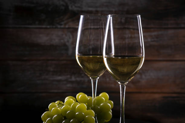istock Two full white wine glasses with grapes on a table on a wooden background 1217371217