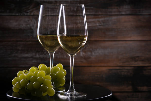 istock Two full white wine glasses with grapes on a table on a wooden background 1217372428