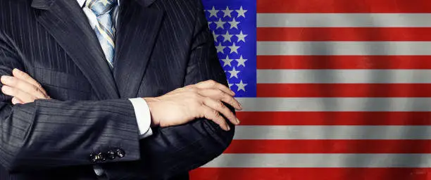 Businessman in a suit with his hands arms crossed on flag background