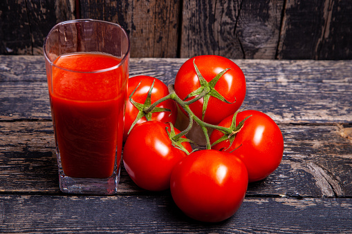 glass of tomato juice and tomatoes on wooden background