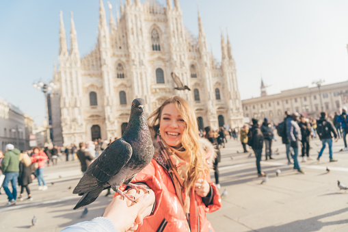 POV image of two girls best friends holding hands and making picture in the square of Milan Cathedral  (duomo di Milano) with dove sitting between them