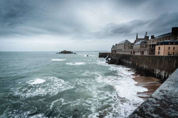 We are on the ramparts of the old town of Saint-Malo\nThe weather is rainy and stormy\nWe are at the top of the ramparts at the level of the beach of Bon Secours\nIn the distance we see the island of Grand Bé and just behind the island of Petit Bé\nIt's a Breton time\nThe tide is rising\non the small island opposite is Fort Nationale