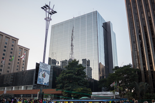 Sao Paulo, SP, Brazil - May 26, 2019: Building with glass facade on Avenida Paulista, reflecting other buildings and a TV tower.