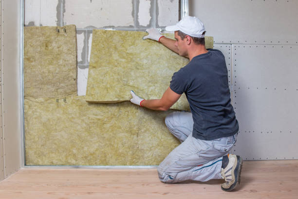 Worker insulating a room wall with mineral rock wool thermal insulation.