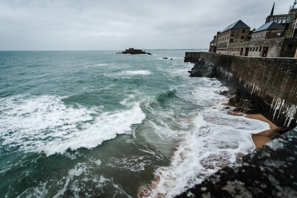 We are on the ramparts of the old town of Saint-Malo\nThe weather is rainy and stormy\nWe are at the top of the ramparts at the level of the beach of Bon Secours\nIn the distance we see the island of Grand Bé and just behind the island of Petit Bé\nIt's a Breton time\nThe tide is rising\non the small island opposite is Fort Nationale