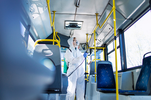 Salud del transporte público. Hombre en traje de protección blanco desinfectando y desinfectando manillares e interiores de bus para dejar de propagar coronavirus altamente contagiosos o COVID-19. photo