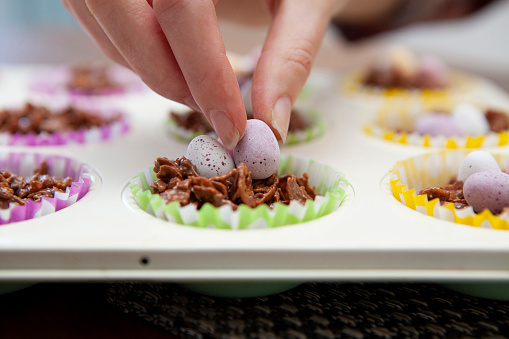 Hand decorating chocolate corn flake cake in a baking tray with a mini chocolate Easter egg