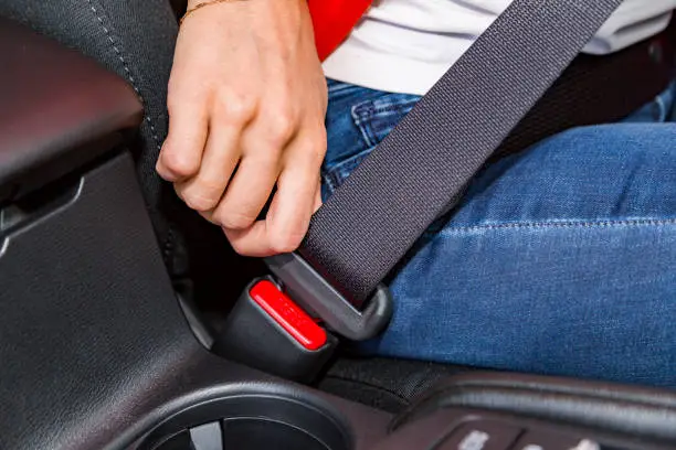 Close up female hand of young woman with bracelet on it fasten seat belt in car