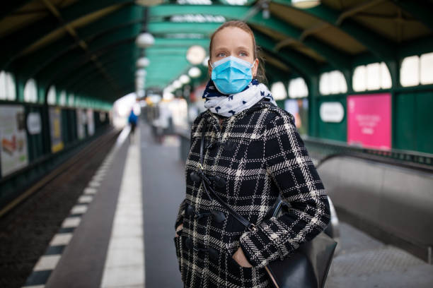 Woman protective face mask on metro station Woman in winter coat with protective mask on face standing on metro station. Female commuter waiting for the train during Covid-19 outbreak. railroad station platform photos stock pictures, royalty-free photos & images