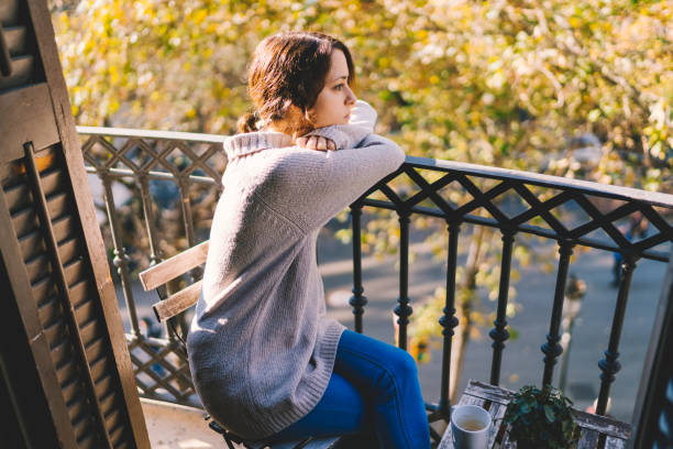 Woman staying at the terrace during pandemic on sunny day feeling worried
